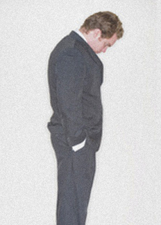 Depressed man with hunched shoulders staring at floor.